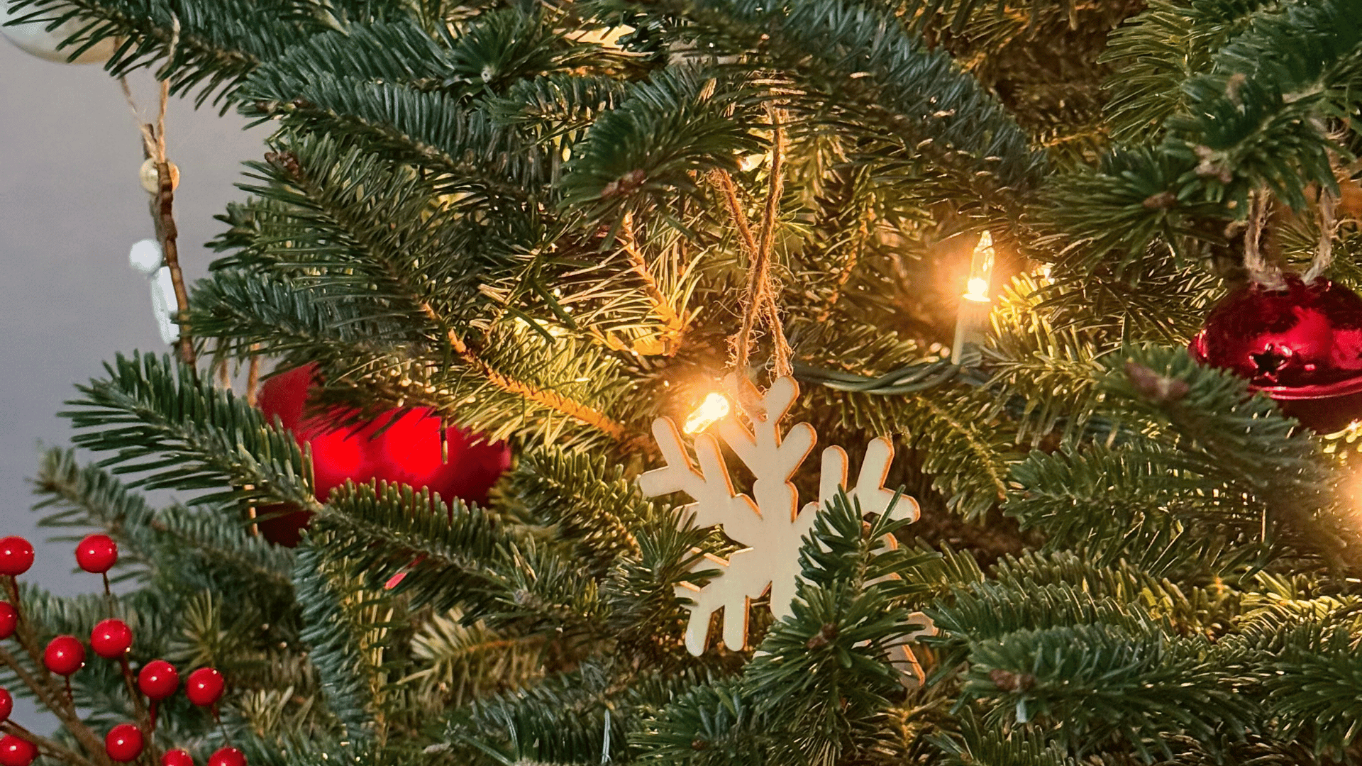 Decorated Christmas tree with red berries, white snowflake ornament, and string lights.